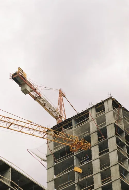 Deux grues jaunes devant un immeuble en béton en cours de construction.